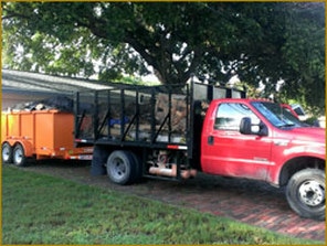 Red ford truck with dump bed on back pulling an orange trailer filled with garbage. Photo taken in clearwater Florida